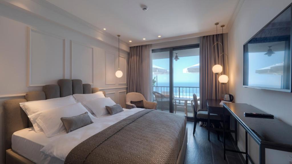 a bedroom with a bed and a desk and a balcony at Vivid Blue Serenity Resort in Sveti Stefan