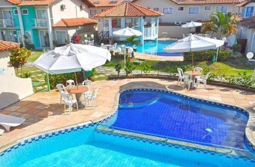 a pool with tables and chairs and umbrellas at Casa 3 Suites Duplex AR Completa Condomínio fechado Moria à 500 m Praia Axe MOI in Porto Seguro