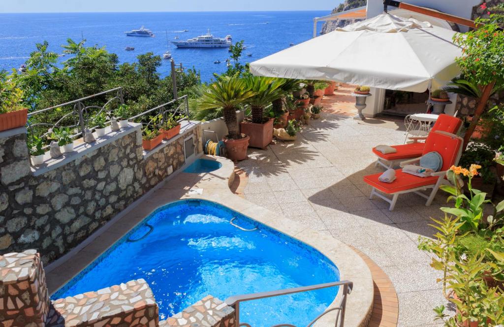 a swimming pool with an umbrella and chairs and the ocean at Villa Teste di Moro in Capri