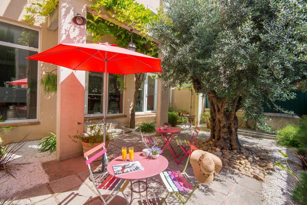 une table et des chaises avec un parapluie rouge à côté d'un arbre dans l'établissement Hotel du Forum, à Carpentras