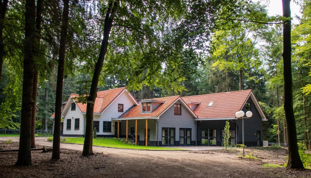 een wit huis met een rood dak en bomen bij Villa Woudstee in Vierhouten