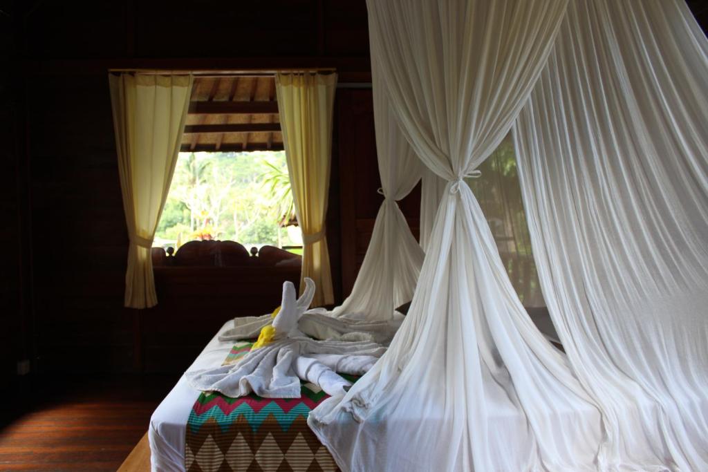 1 cama con cortinas blancas en un dormitorio en Pondok Tepi Sungai, en Sidemen