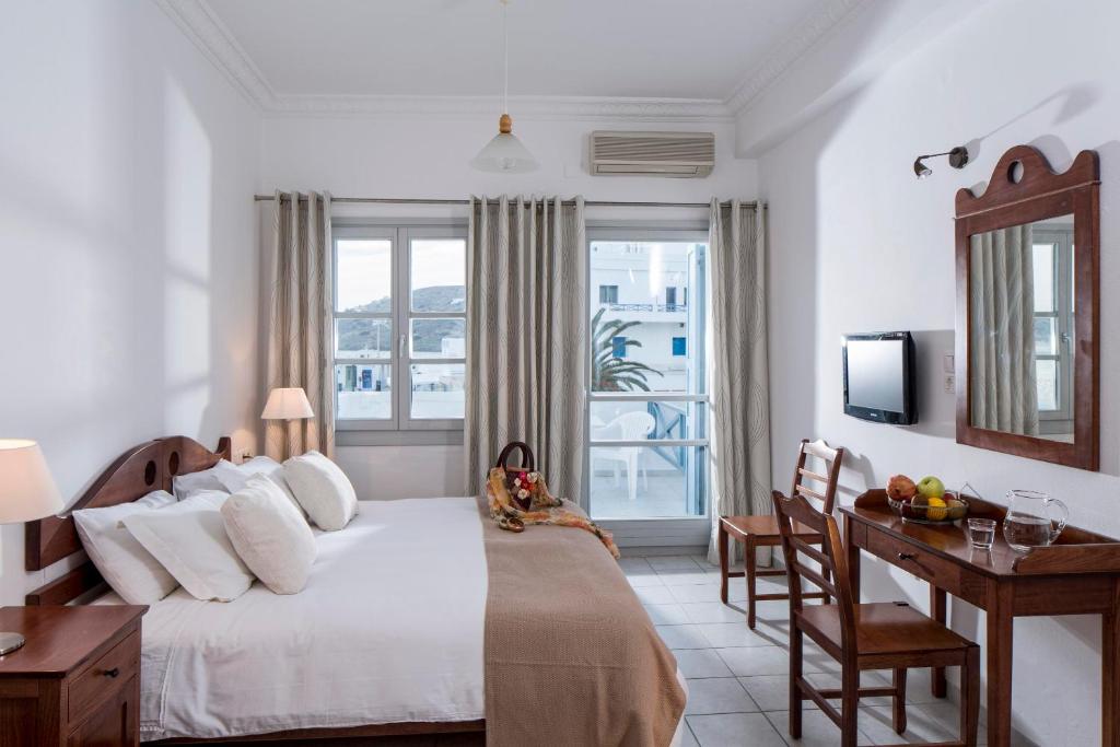 a bedroom with a bed and a desk and a window at Acteon Hotel in Ios Chora