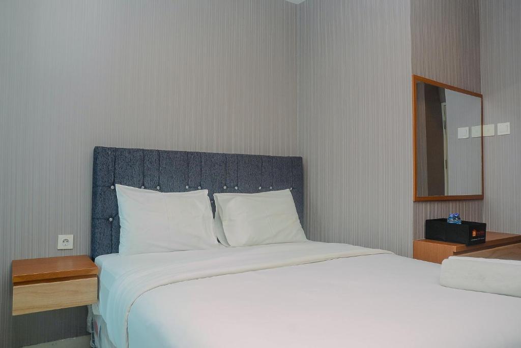 a bedroom with a large white bed with a blue headboard at Comfortable Studio Grand Kamala Lagoon Apartment By Travelio in Pekayon Satu