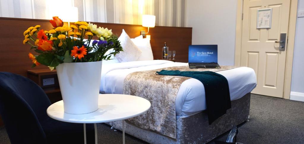 Un dormitorio con una cama con un jarrón de flores y un ordenador portátil en The Gate Hotel, en Dublín