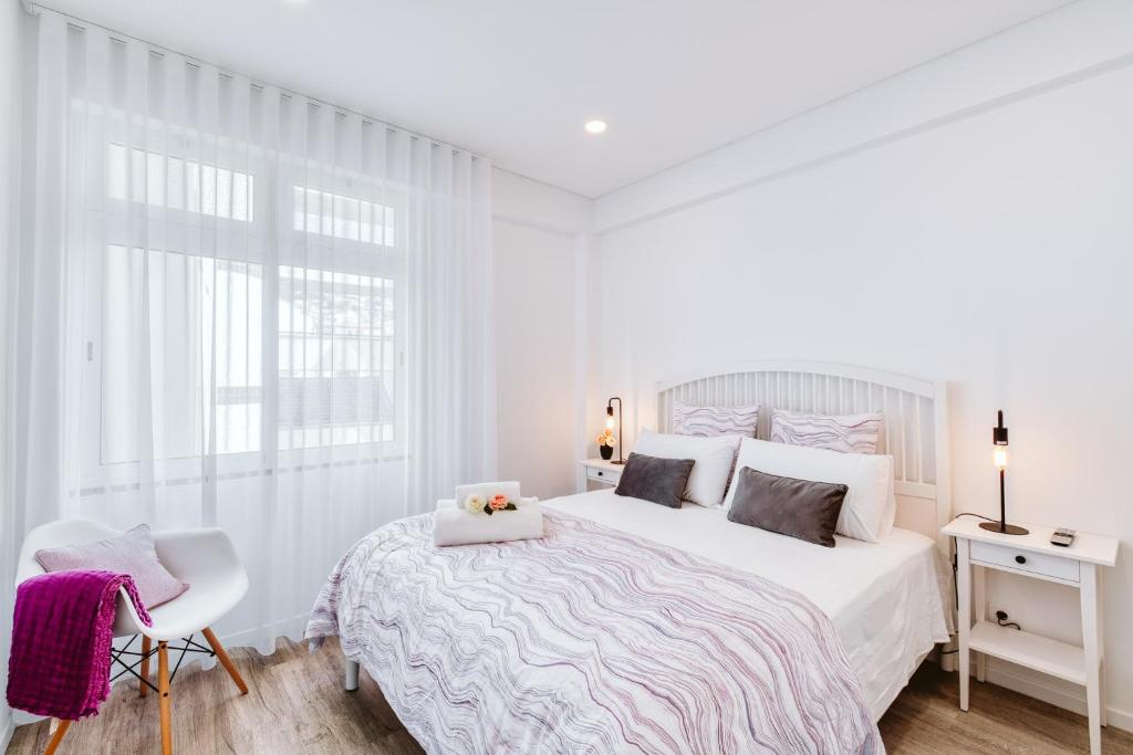 a white bedroom with a large bed and a chair at Os Fragosinhos in Funchal