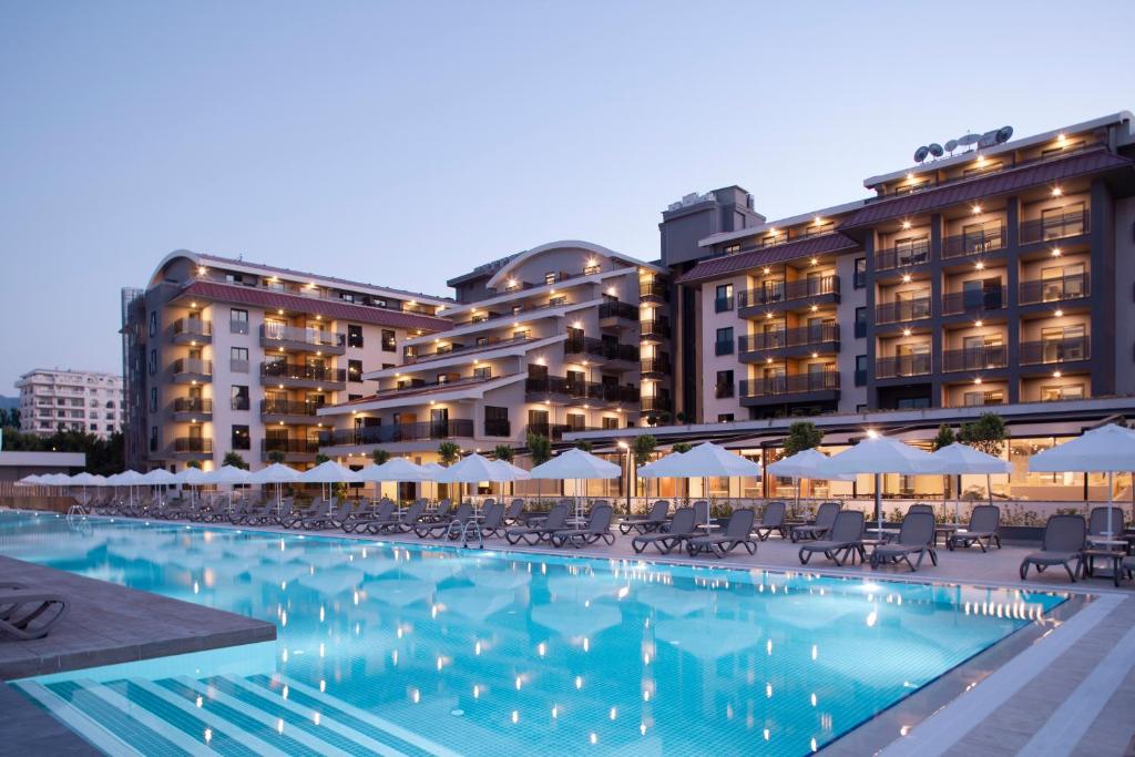 a pool with chairs and umbrellas in front of a hotel at Green Garden Resort & Spa Hotel in Alanya