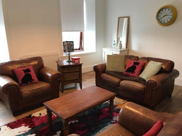 a living room with leather furniture and a clock on the wall at Centrally located 2 bed modern flat with harbour views in Wick
