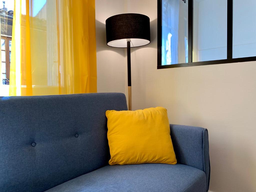 a blue couch with a yellow pillow next to a lamp at Appartements Voltaire - Carcassonne Centre in Carcassonne