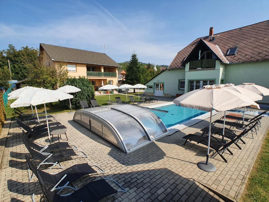 a pool with chairs and umbrellas next to a house at Krisztián Apartmanház in Vonyarcvashegy