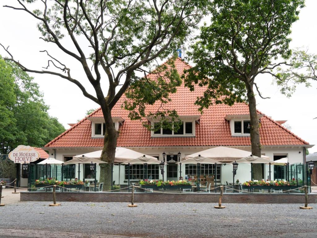 un bâtiment avec des tables et des parasols devant lui dans l'établissement Auberge De Moerse Hoeve, à De Moer