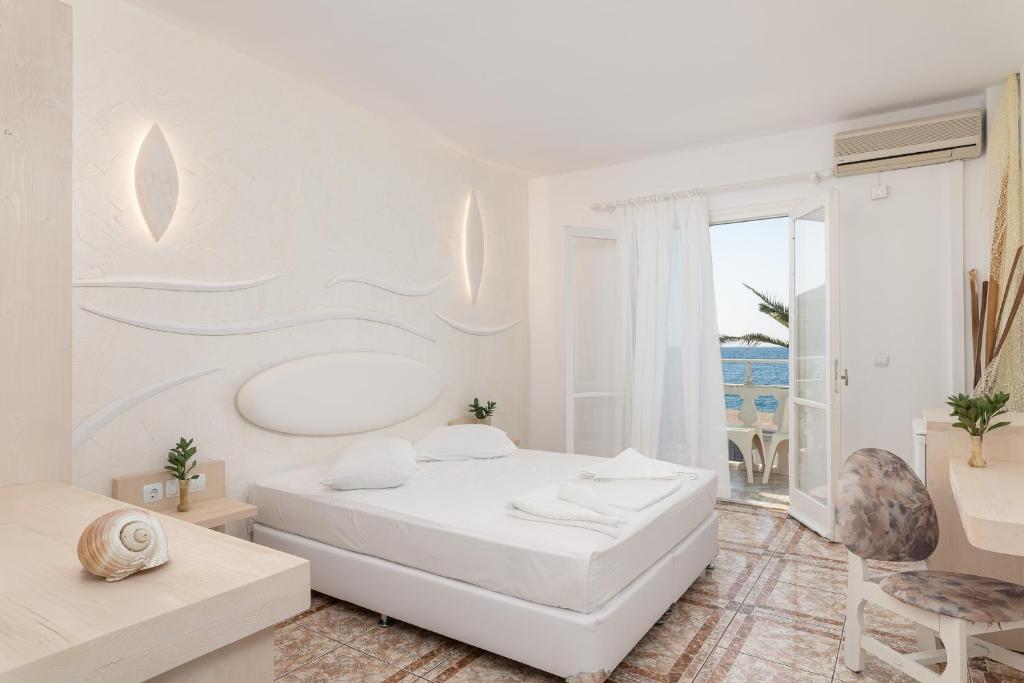 a white bedroom with a bed and a balcony at Kokkari Beach Hotel in Kokkari