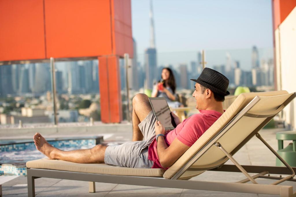 un homme assis sur une chaise longue avec un ordinateur portable dans l'établissement URBAN Al Khoory Hotel, à Dubaï