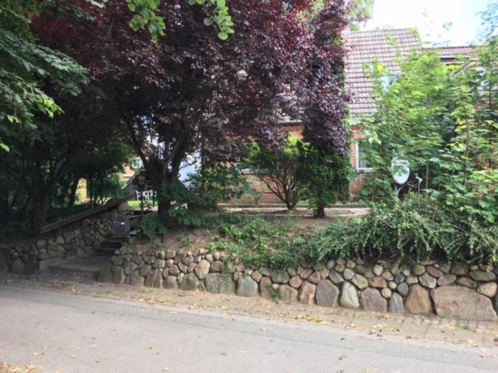 a stone retaining wall with trees and a building at Mühlenweg- Tante Lise in Süderlügum