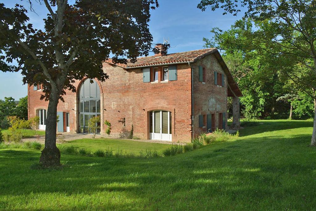an old brick house with a tree in a field at La Bastide rouge in Saint-Geniès-Bellevue