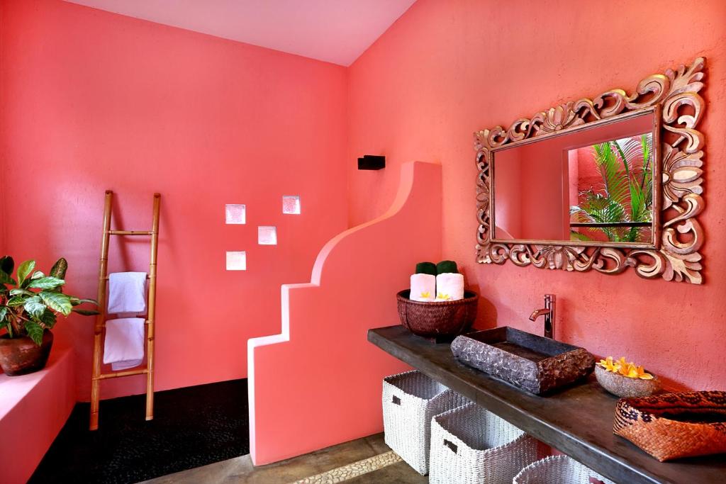 een badkamer met een rode muur met een spiegel en een wastafel bij PinkCoco Uluwatu - Constant Surprises & for Cool Adults Only in Uluwatu