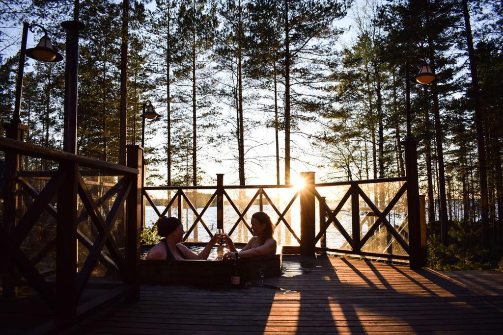 Due donne sedute su un ponte con il sole sullo sfondo di Puruvesi Holiday Villas, Kalliohovi a Hiukkajoki