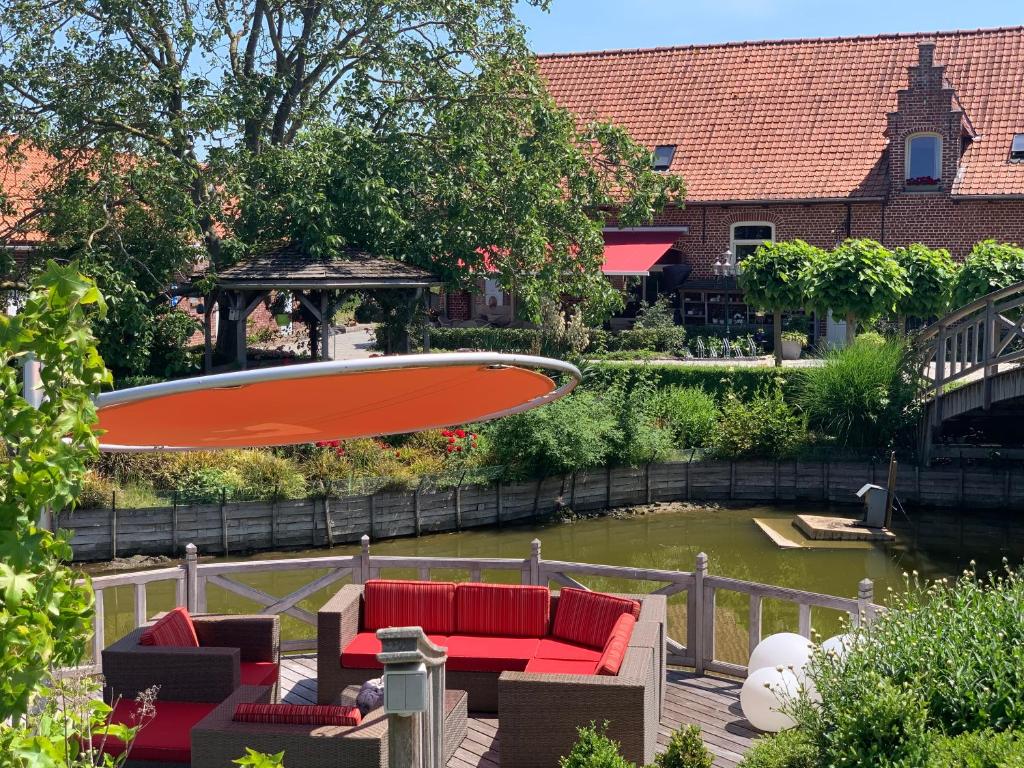 um guarda-chuva sobre um pátio com mobiliário vermelho e uma lagoa em B&B De Rentmeesterhoeve em Reningelst