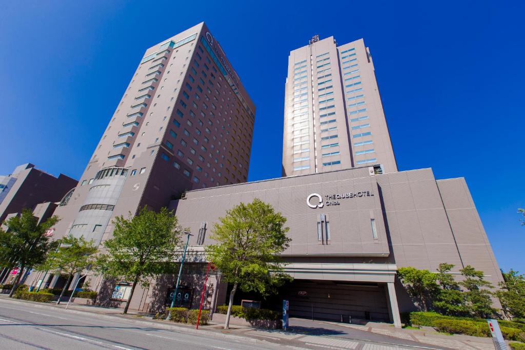 two tall buildings on a city street with trees at The QUBE Hotel Chiba in Chiba