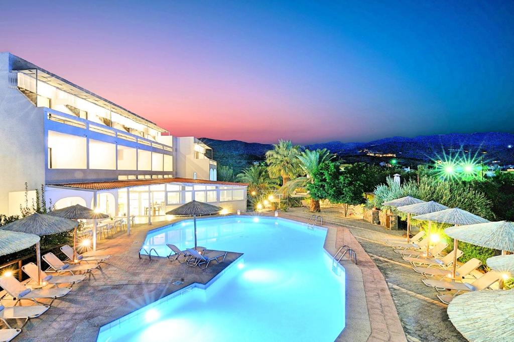 a pool in front of a building with chairs and umbrellas at Elounda Krini Hotel in Elounda