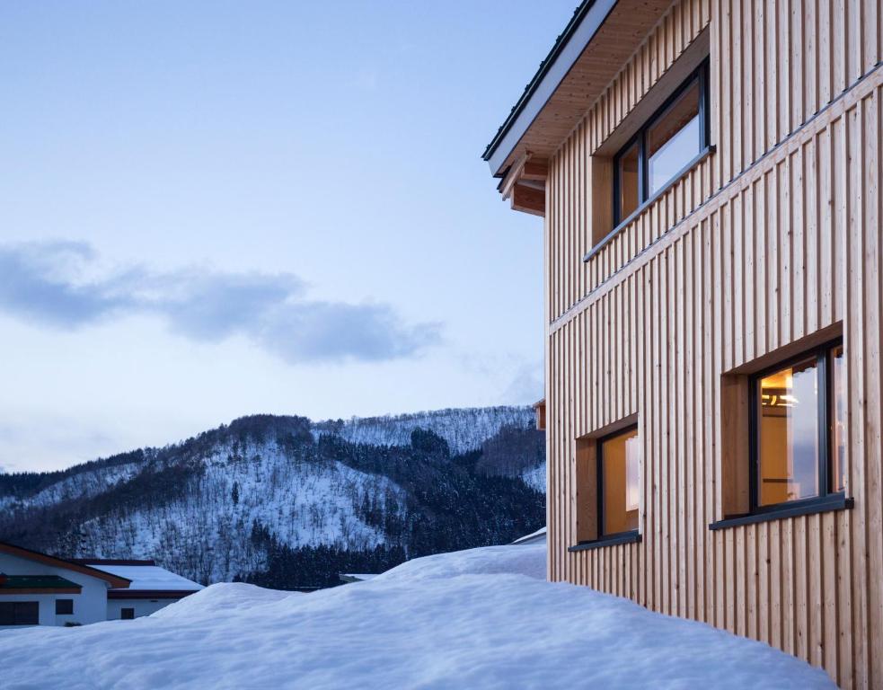 un edificio en la nieve con montañas en el fondo en Tamanegi House luxury 4 bedroom Ski Chalet, en Nozawa Onsen