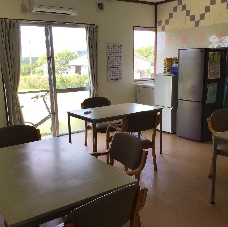 a kitchen with two tables and a refrigerator and chairs at Shimaotoya in Iriomote