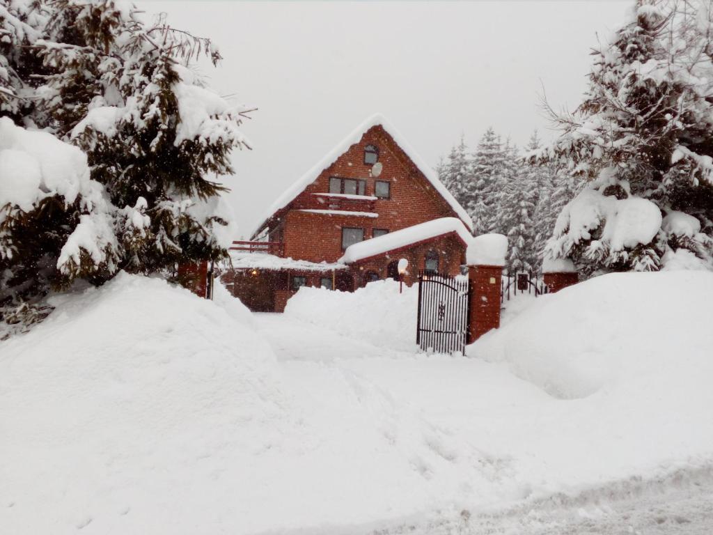 Górski Zakątek z kominkiem i tarasem في Laliki: منزل مغطى بالثلج مع بوابة