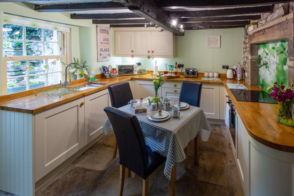 een keuken met een tafel en stoelen en een keuken met witte kasten bij Poppy Cottage in Grassington