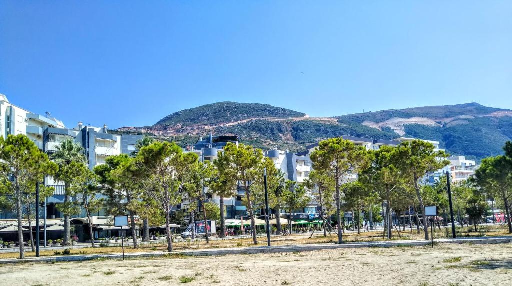 une rangée d'arbres devant les bâtiments et les montagnes dans l'établissement Oslo Apartments - Albania, à Vlorë