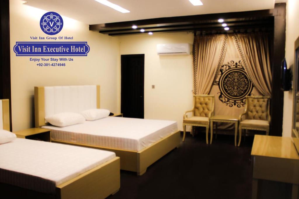 een kamer met 2 bedden en een bord waarop staat: Visit Inn Executive Hotel bij Hotel Visit Inn Executive in Lahore