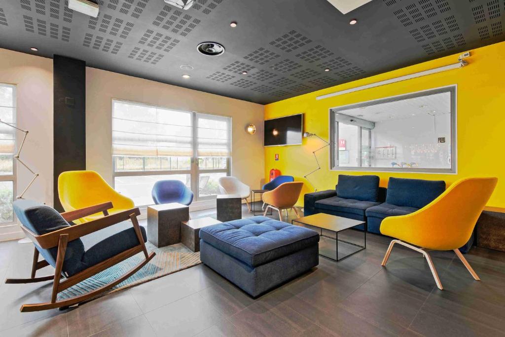 a living room with yellow and blue chairs and a couch at Campanile Roissy - Aéroport CDG - Le Mesnil Amelot in Le Mesnil-Amelot