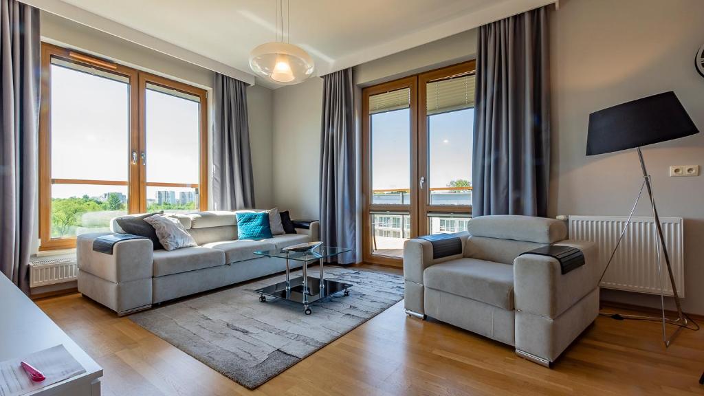 a living room with a couch and two chairs and windows at VacationClub - Olympic Park Apartment A604 in Kołobrzeg