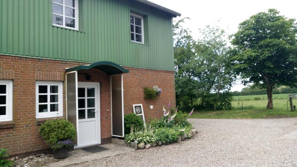 ein grünes Gebäude mit einer weißen Tür und Blumen in der Unterkunft Ferienwohnung Thomsen in Tarp