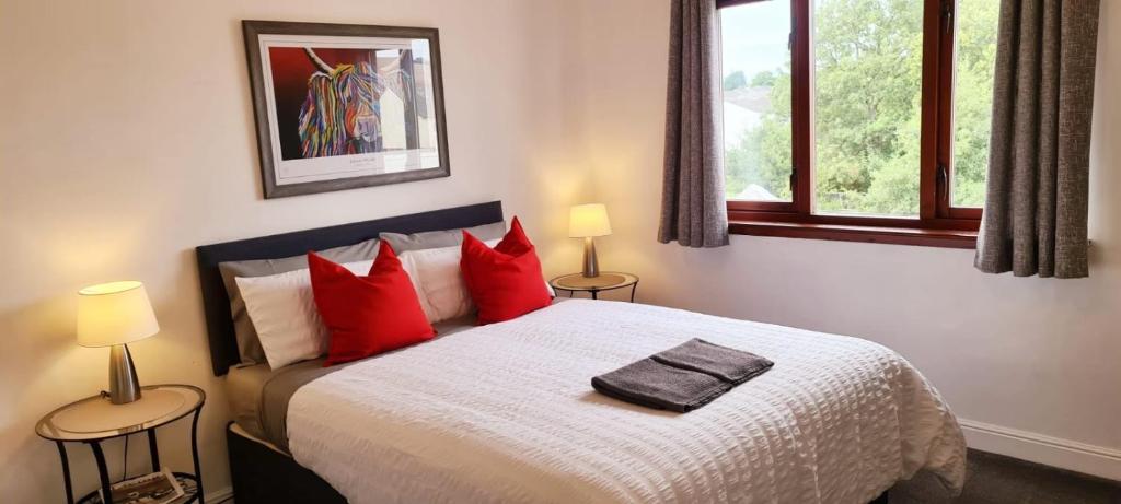 a bedroom with a bed with red pillows and two lamps at Levenhowe Holiday Apartment in Balloch