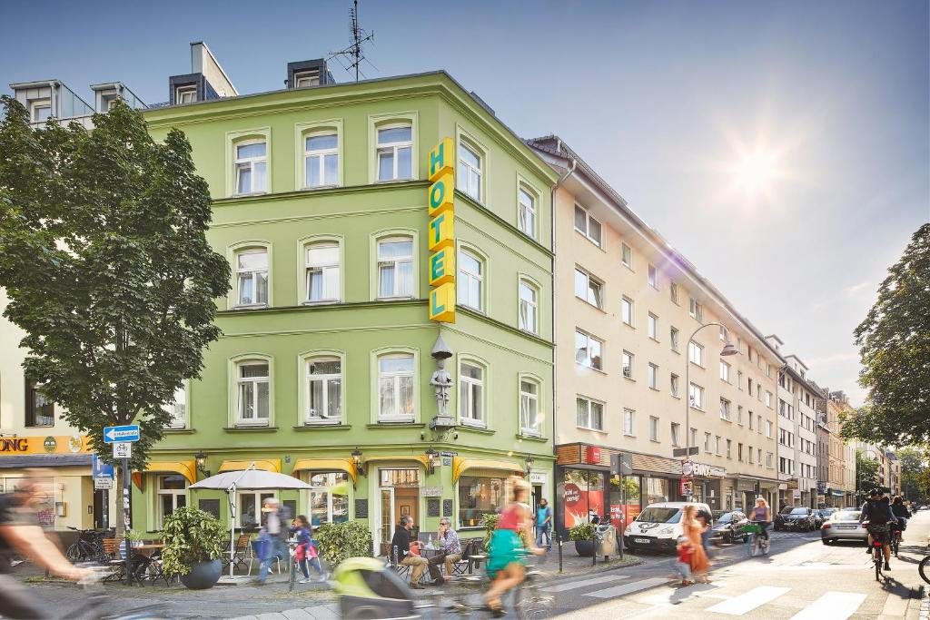 a green building on a busy city street with people at Hotel am Chlodwigplatz in Cologne