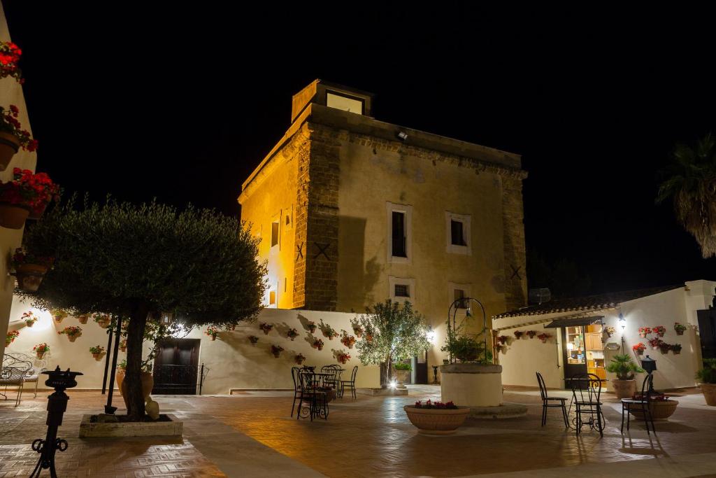 a building with tables and chairs in a courtyard at night at Hotel Foresteria Baglio Della Luna in San Leone