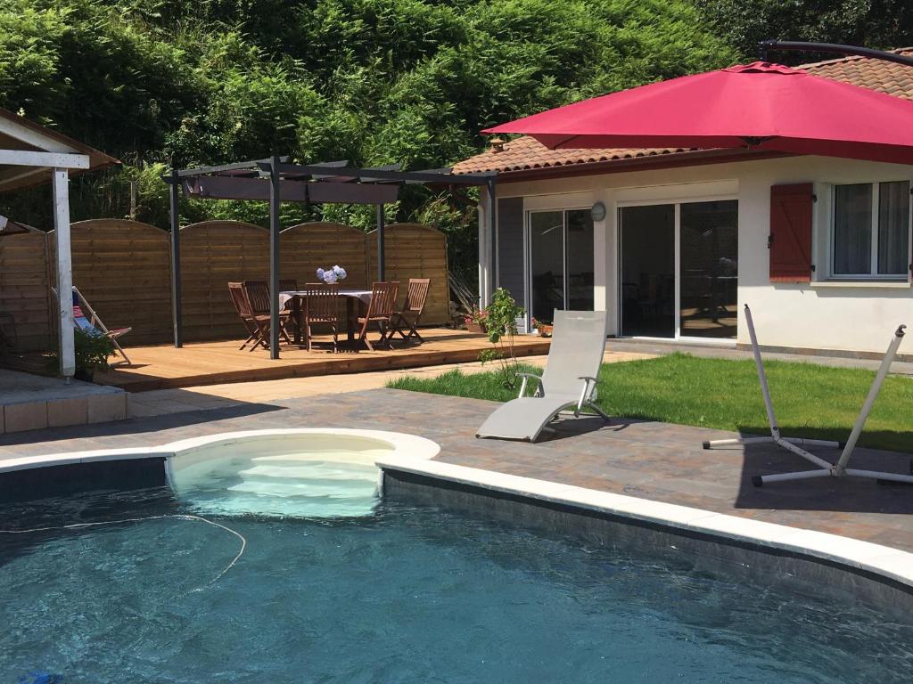 una piscina con una mesa y una sombrilla roja en gîte au Pays Basque entre mer et montagne, en Villefranque