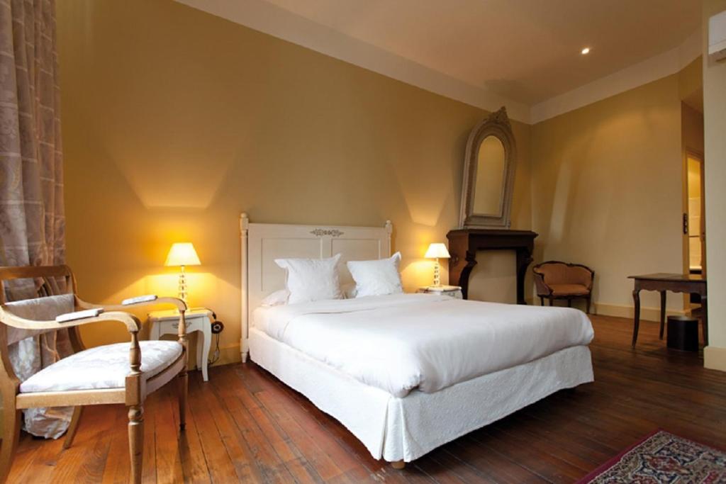 a bedroom with a large white bed and a chair at Hostellerie du Coq d'Or in Jonzac