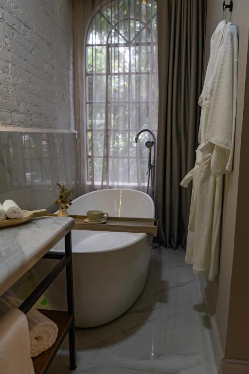 A freestanding soaking tub sits beside a tall window, with robes and a small bath tray.