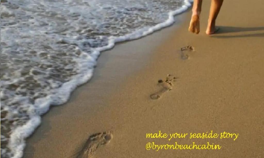 een persoon die op het strand loopt met voetafdrukken in het zand bij Byron Beach Cabin in Byron Bay