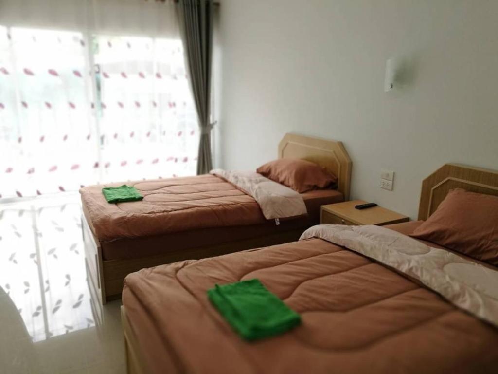 - une chambre avec 2 lits avec des draps verts et une fenêtre dans l'établissement บ้านพักณัฐรินีย์, à Sam Phran