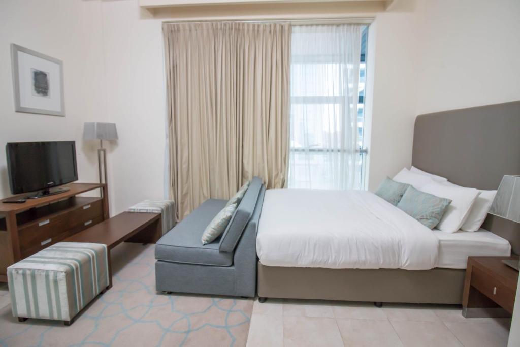 a bedroom with a bed and a couch and a television at Spacious Studio - Sports city - Diamond in Dubai