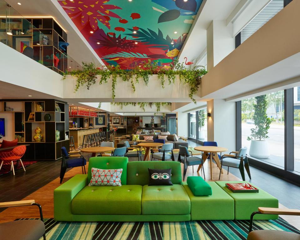 a library with a green couch and tables and chairs at citizenM Kuala Lumpur Bukit Bintang in Kuala Lumpur