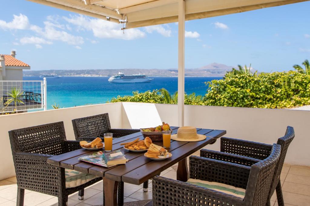 a table with food and chairs on a balcony with the ocean at Manos Apartments in Almirida