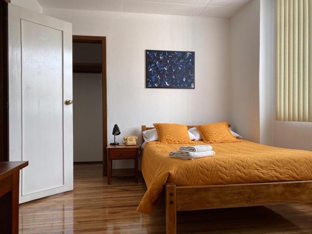 Schlafzimmer mit einem Bett mit orangefarbener Bettwäsche und einem Tisch in der Unterkunft Hotel 9 de Octubre in Quito