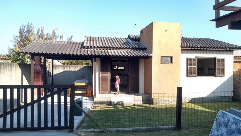 a house with a gate and a woman standing in front of it at Casa bege Bal Arroio do Silva com internet in Arroio do Silva