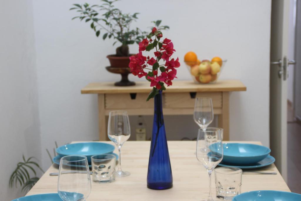 a table with a blue vase with red flowers and glasses at Celia House in Las Palmas de Gran Canaria