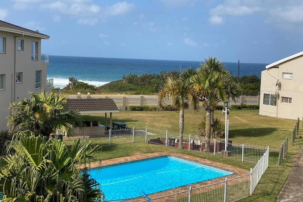 a swimming pool in front of a house and the ocean at Uvongo Chalets 12 in Margate