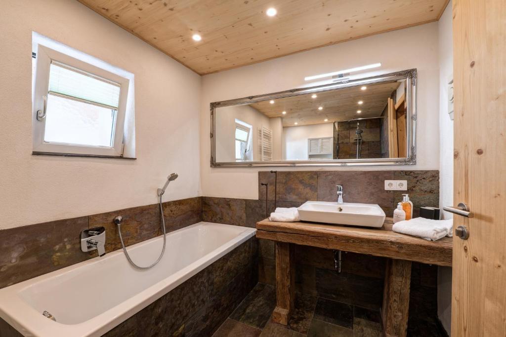 a bathroom with a tub and a sink and a mirror at Quality Hosts Arlberg - ALPtyrol Appartements in Sankt Anton am Arlberg