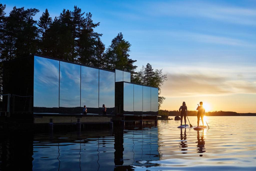twee mensen op surfplanken in het water bij zonsondergang bij Lake Hotel Lehmonkärki - Haasi Mirror Houses in Asikkala